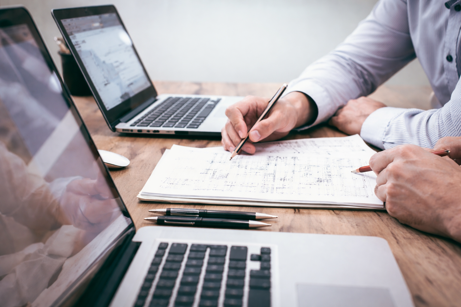 Profissionais analisando projetos estruturais em mesa de trabalho com notebooks e plantas técnicas, representando consultoria estrutural online.